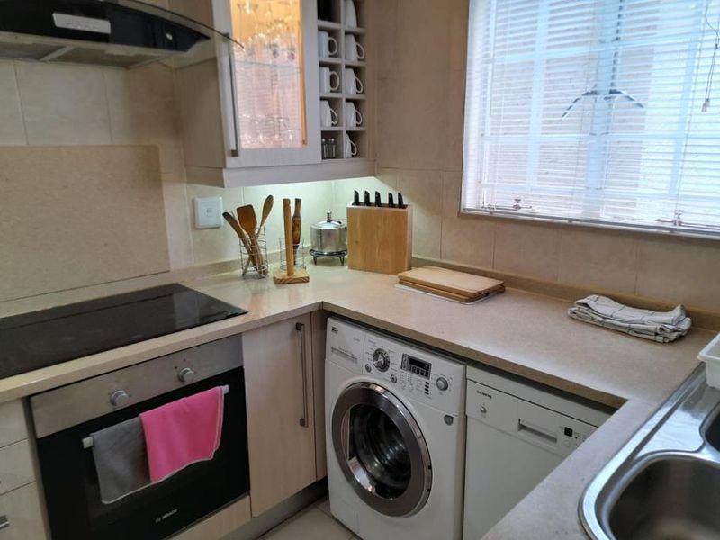 A functional kitchen featuring built-in cabinetry, integrated oven and hob, extractor fan, and a stainless steel sink with tiled backsplash and natural light.