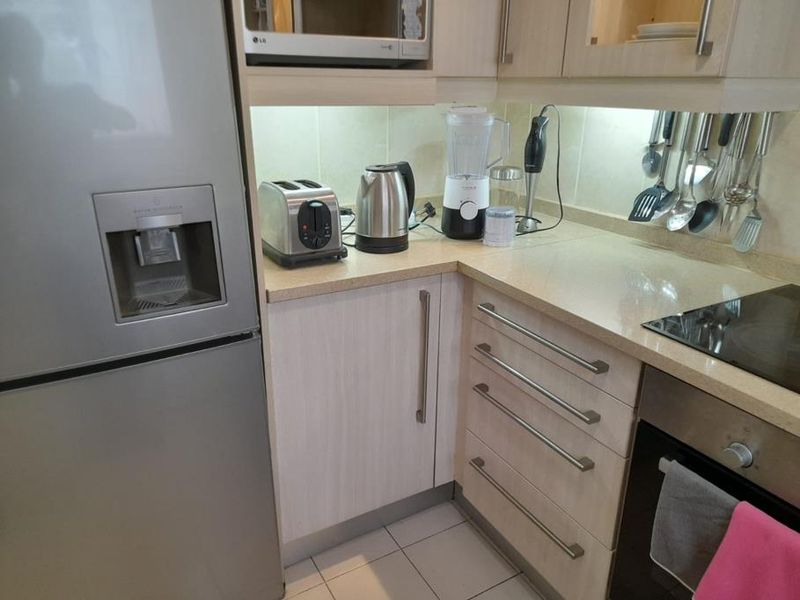 A functional kitchen area featuring light-toned laminate cabinetry, stone countertops, a built-in oven, and an electric hob with integrated under-cabinet lighting.