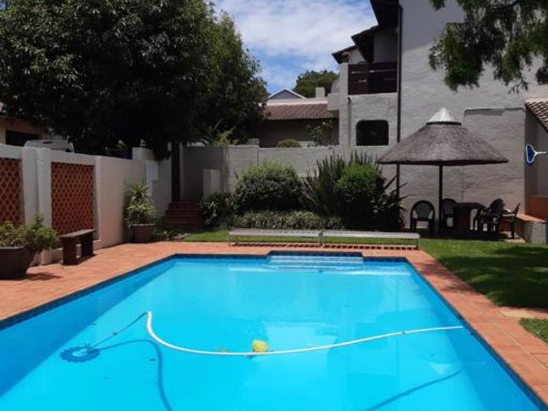 A private outdoor swimming pool area featuring brick paving, a boundary wall, and a thatched umbrella, set within a landscaped garden environment.