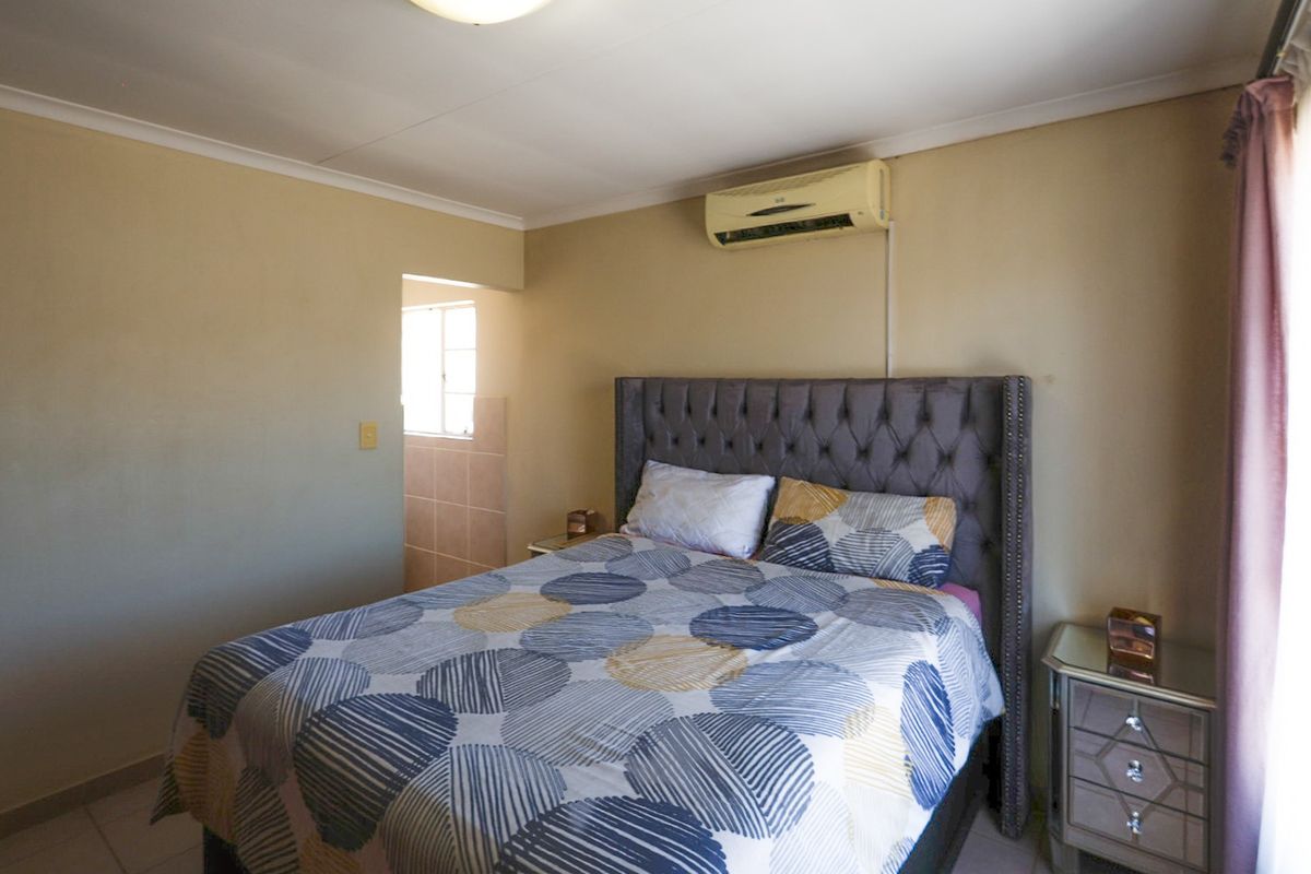 A bedroom featuring tiled flooring, cove cornicing, and a wall-mounted air conditioning unit, with an adjacent tiled area visible.