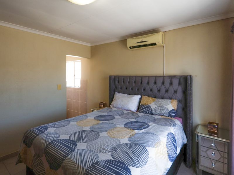 A bedroom featuring tiled flooring, cove cornicing, and a wall-mounted air conditioning unit, with an adjacent tiled area visible.