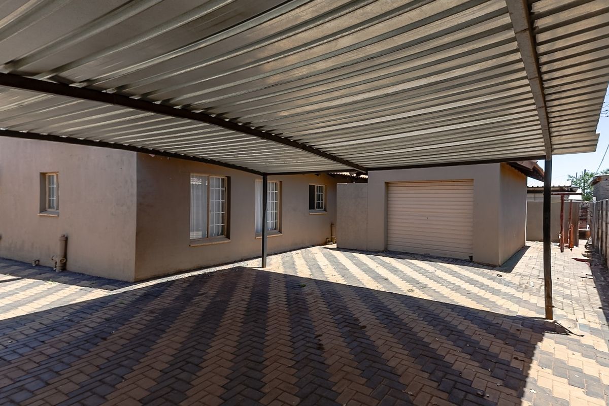 Rear exterior view featuring a large corrugated metal carport, paved driveway, and a secure roll-up garage door attached to the main dwelling.