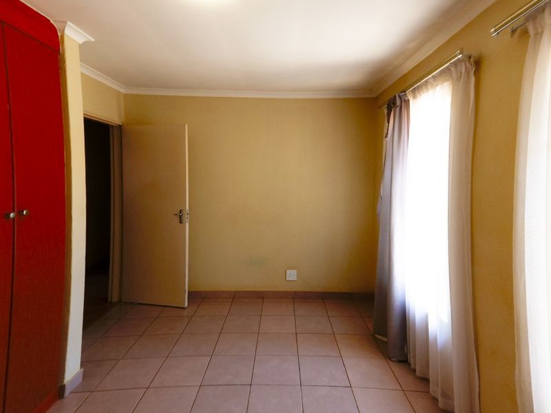 An empty bedroom featuring tiled flooring, a built-in wardrobe, and neutral wall finishes, offering a blank canvas for personalization.