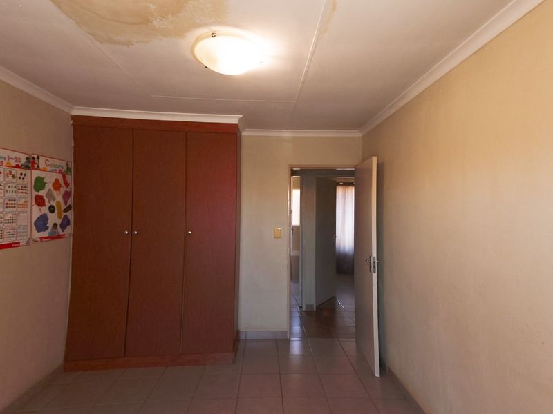 A bedroom featuring tiled flooring and a built-in wardrobe, showing visible water damage on the ceiling.