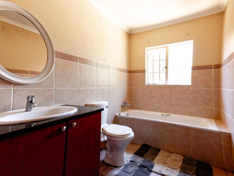 A functional bathroom featuring a vanity cabinet with basin, a standard toilet, and a tiled bathtub area with natural light from the window.