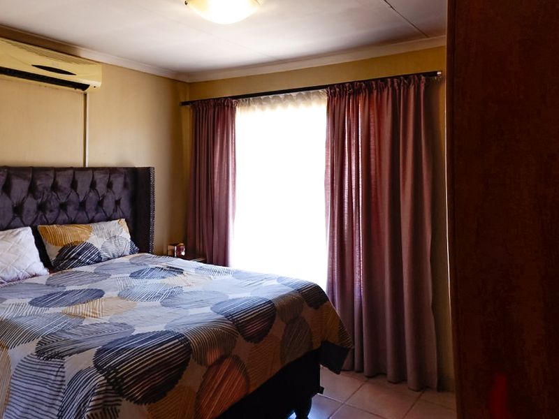 A bedroom featuring tiled flooring and a wall-mounted air conditioning unit, with natural light entering through a window dressed with curtains.