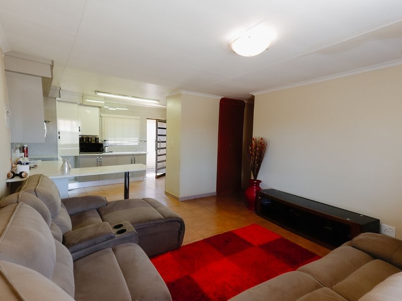 Open-plan living area featuring a functional kitchen with breakfast bar, tiled flooring, and neutral walls, offering a versatile space for daily living.