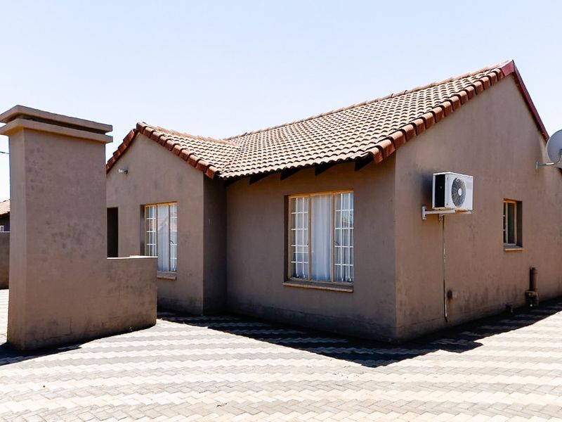 Rear view of a single-story house featuring a tiled roof, paved driveway, and exterior air conditioning unit.