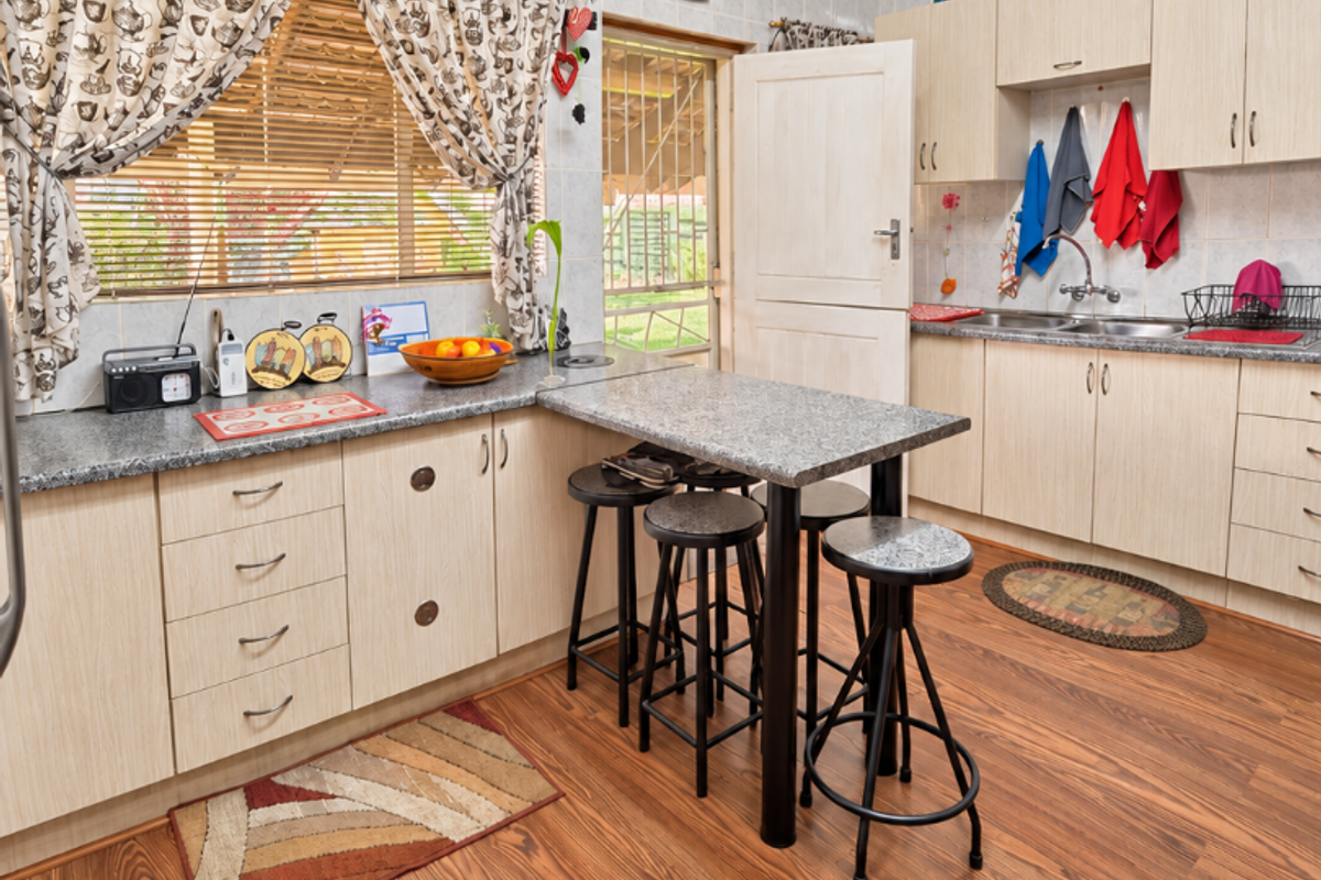 A functional kitchen featuring light wood-tone cabinetry, granite countertops, a breakfast bar, and durable laminate flooring with a tiled splashback.
