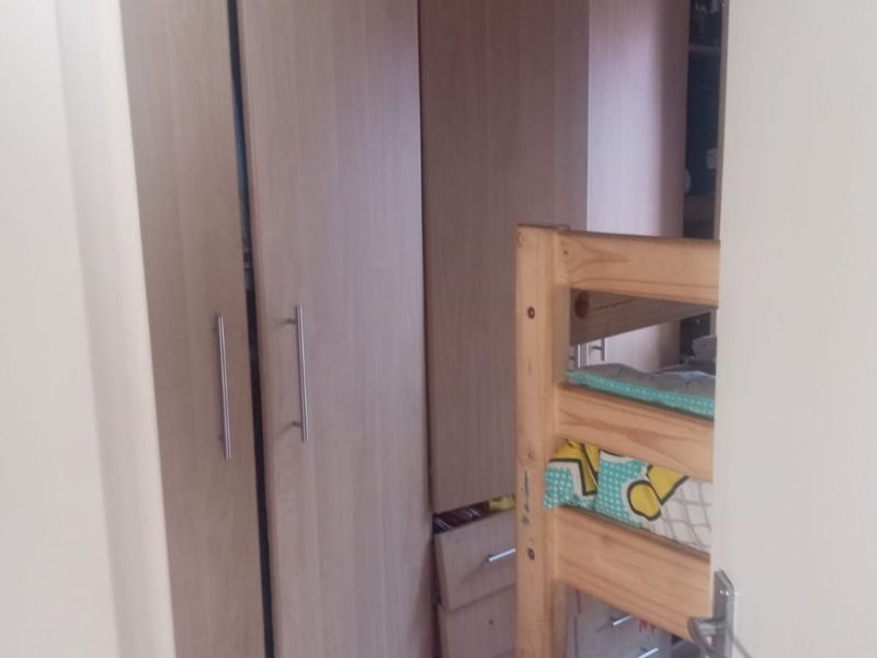 A bedroom featuring light wood-toned built-in wardrobes and tiled flooring, viewed through a doorway.