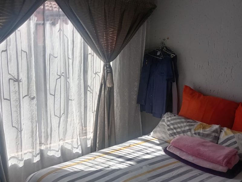 A bedroom featuring tiled flooring and textured wall finishes, illuminated by natural light through a window with draped curtains.