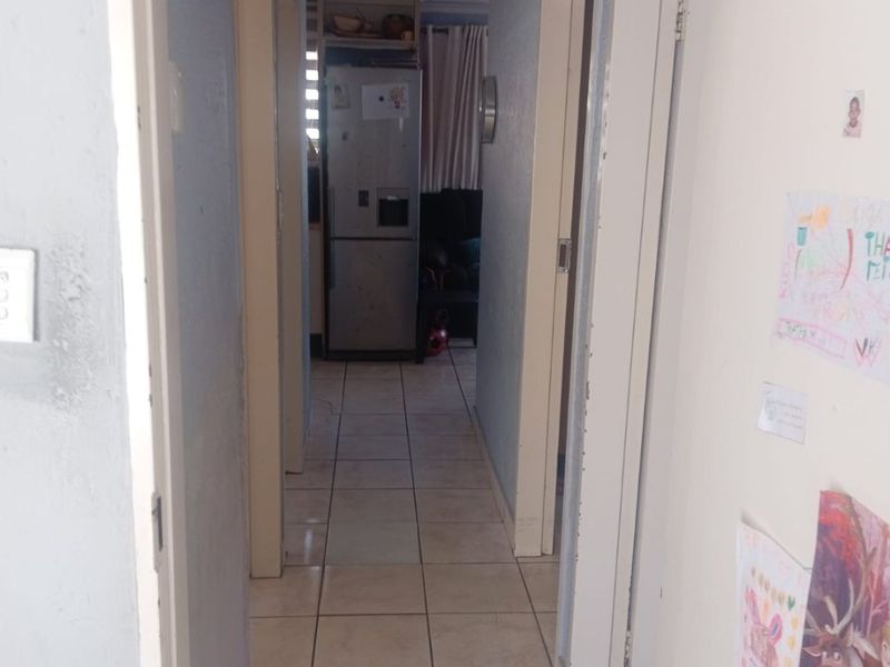 A narrow residential hallway featuring tiled flooring and access to multiple rooms, showing signs of wear and requiring cosmetic updates.