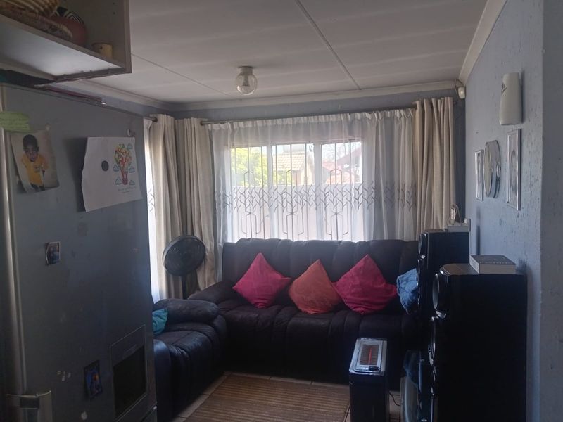 A compact living room featuring tiled flooring and natural light through a window with curtain rails.