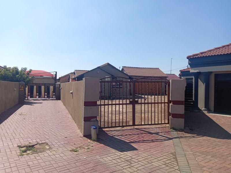Front exterior view of the property featuring a paved driveway, boundary wall, and metal security gate entrance.