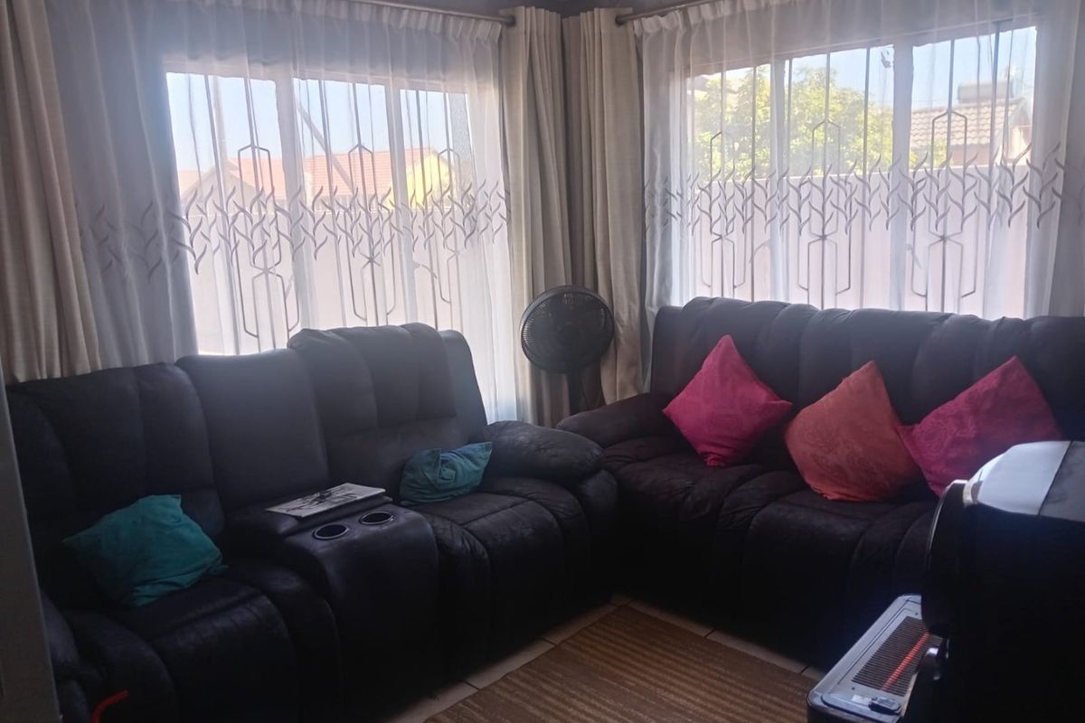 A living room area featuring tiled flooring and large windows with curtain rails, providing natural light to the space.