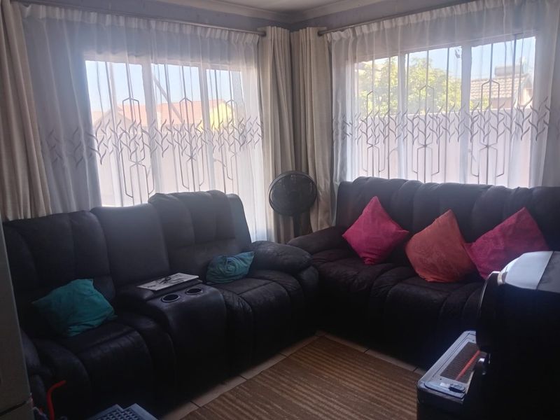 A living room area featuring tiled flooring and large windows with curtain rails, providing natural light to the space.