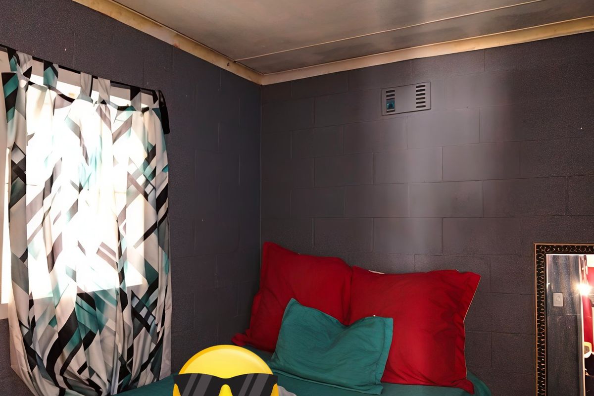 A bedroom featuring dark painted blockwork walls and an unfinished ceiling edge, requiring cosmetic attention to improve the overall finish.