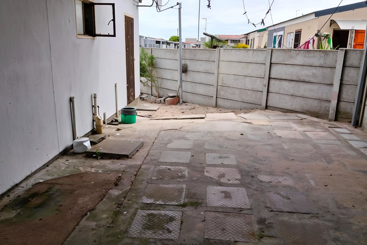 A rear courtyard area featuring a precast concrete boundary wall and paved flooring, requiring maintenance and landscaping to improve the outdoor space.