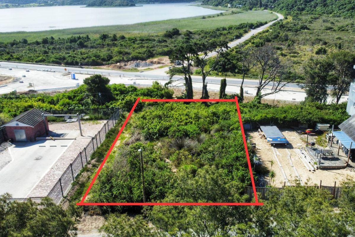An aerial view of a vacant residential plot, clearly marked with red boundary lines, situated near a road and natural landscape.