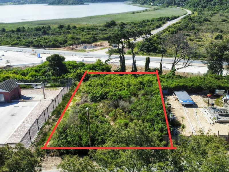 An aerial view of a vacant residential plot, clearly marked with red boundary lines, situated near a road and natural landscape.