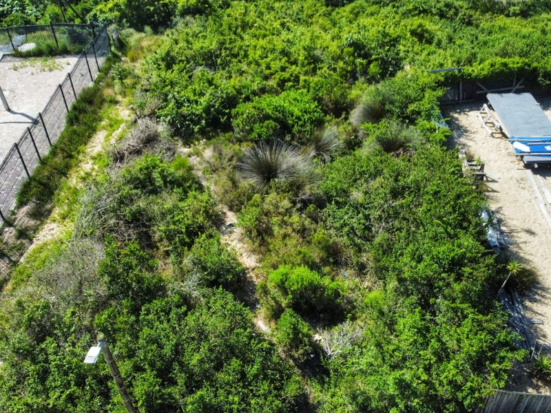 Aerial view of a vacant residential plot featuring dense natural vegetation and a partially cleared sandy section with perimeter fencing.