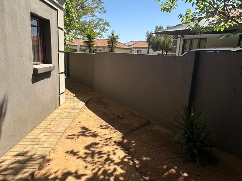 A side exterior view of the property featuring a paved walkway alongside a boundary wall with visible structural cracking.