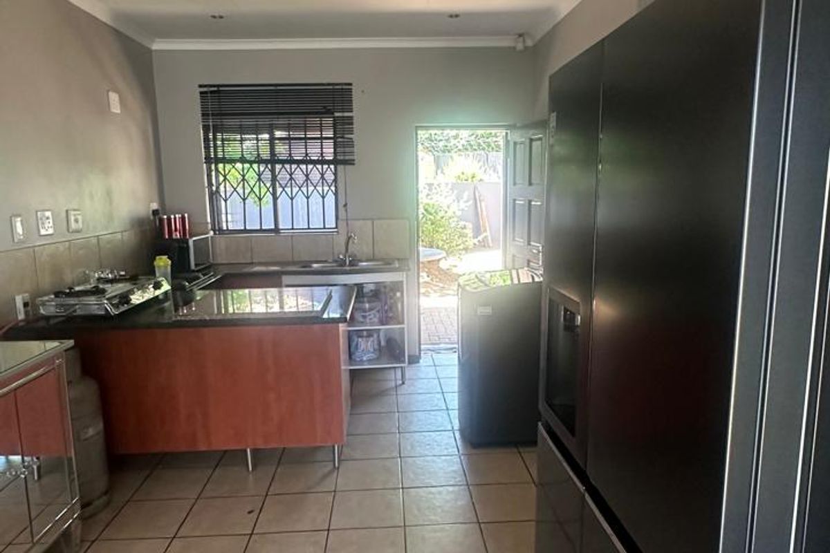 A functional kitchen featuring tiled flooring, granite countertops, built-in cabinetry, and direct access to the rear exterior through a security door.