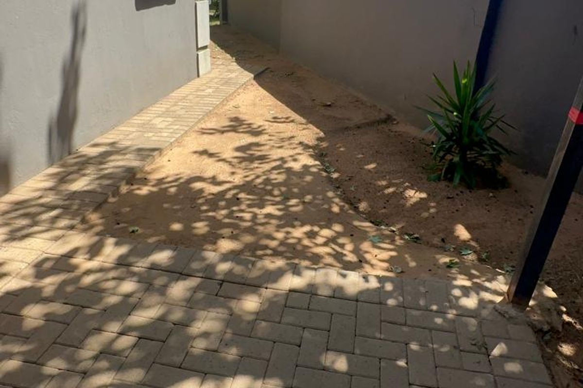 A side passage of the house featuring paved walkways and a boundary wall, providing access to the rear garden area.
