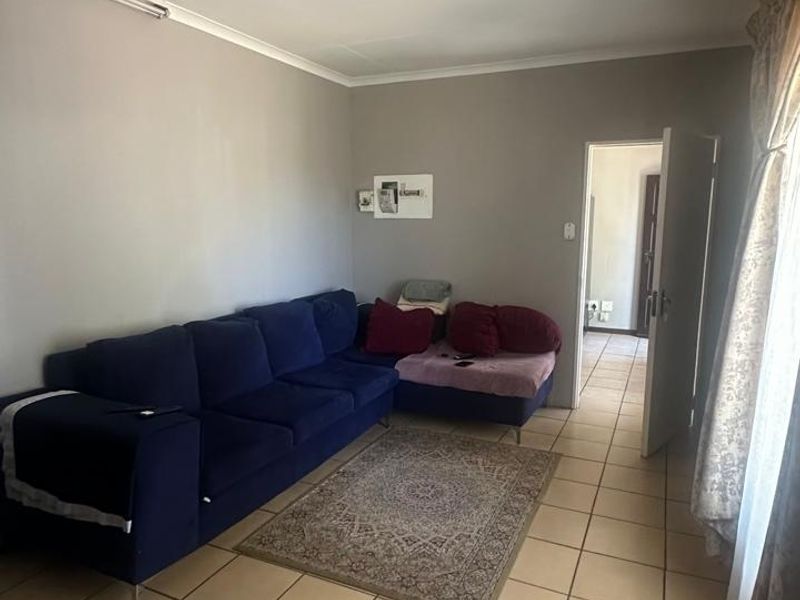 A living room featuring neutral wall paint, tiled flooring, and coved ceiling details, providing a functional space with access to an adjoining hallway.