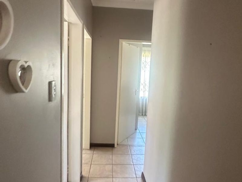A functional hallway featuring neutral tiled flooring and a ceiling access hatch, providing access to multiple rooms within the home.