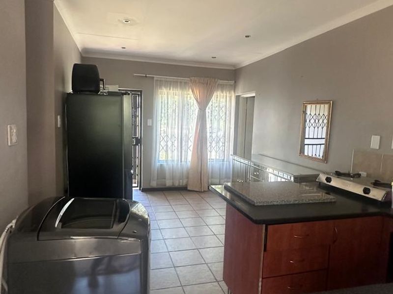 Open plan kitchen and living area featuring tiled flooring, granite countertops, and ample cabinetry, leading towards a bright window with security gate access.