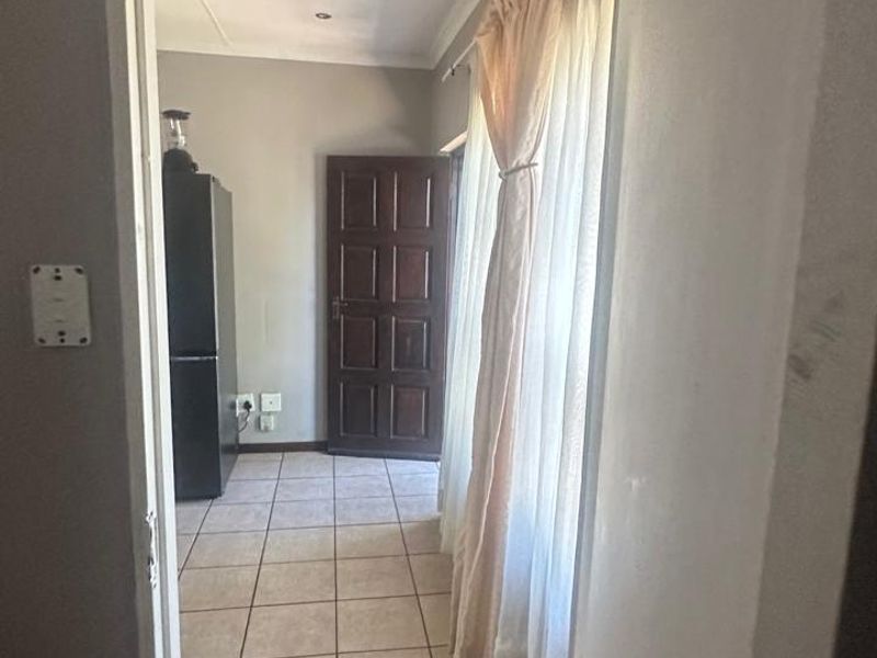 A functional hallway featuring neutral tiled flooring, recessed downlighting, and a classic timber door leading to an adjacent room.