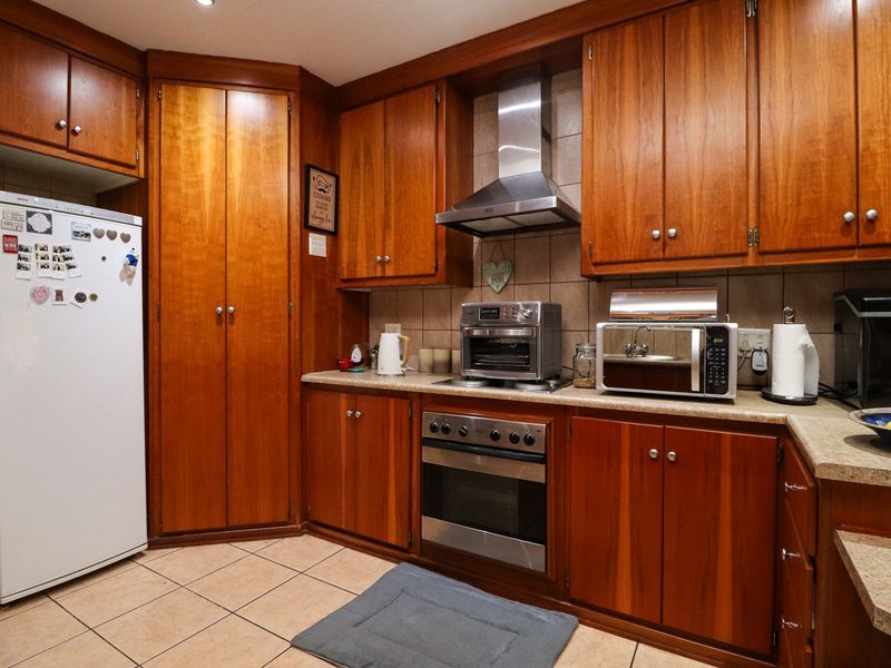 A functional kitchen featuring warm-toned wooden cabinetry, laminate countertops, a tiled backsplash, and integrated stainless steel oven and extractor fan.