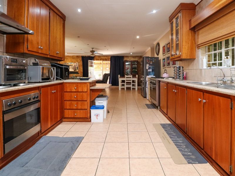 Spacious open-plan kitchen featuring warm-toned wooden cabinetry, tiled flooring, and integrated appliances, flowing seamlessly into the adjacent dining and living areas.