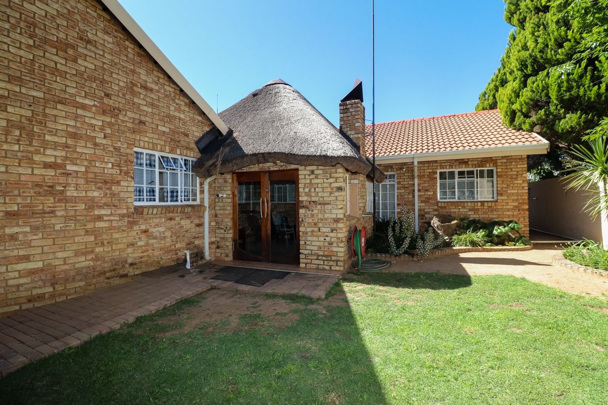 Rear exterior view of the townhouse featuring a combination of face brick walls, a thatched roof section, a tiled roof, and a paved patio area.