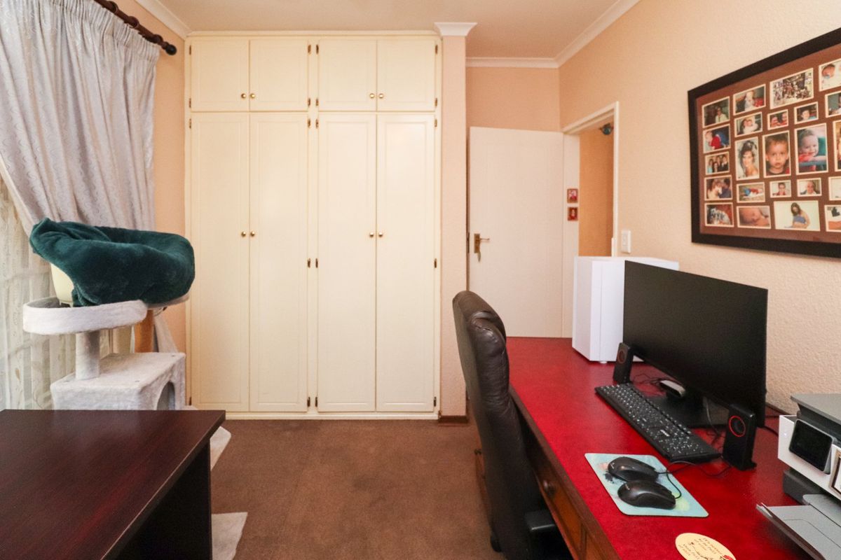 A bedroom featuring built-in cupboards, carpeted flooring, and decorative cornice detailing, currently utilized as a home office space.