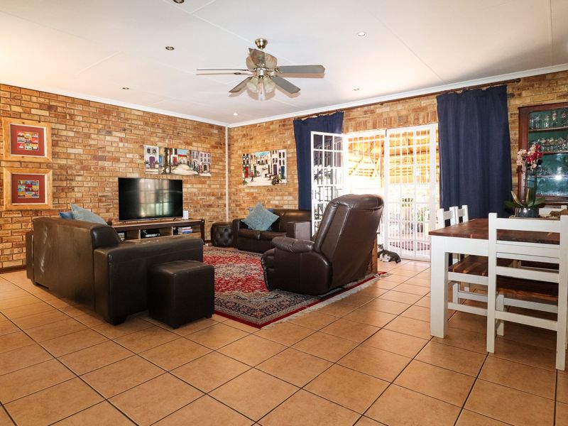 Spacious open-plan living and dining area featuring exposed brick walls, tiled flooring, and direct access to the outdoor patio through double glass doors.
