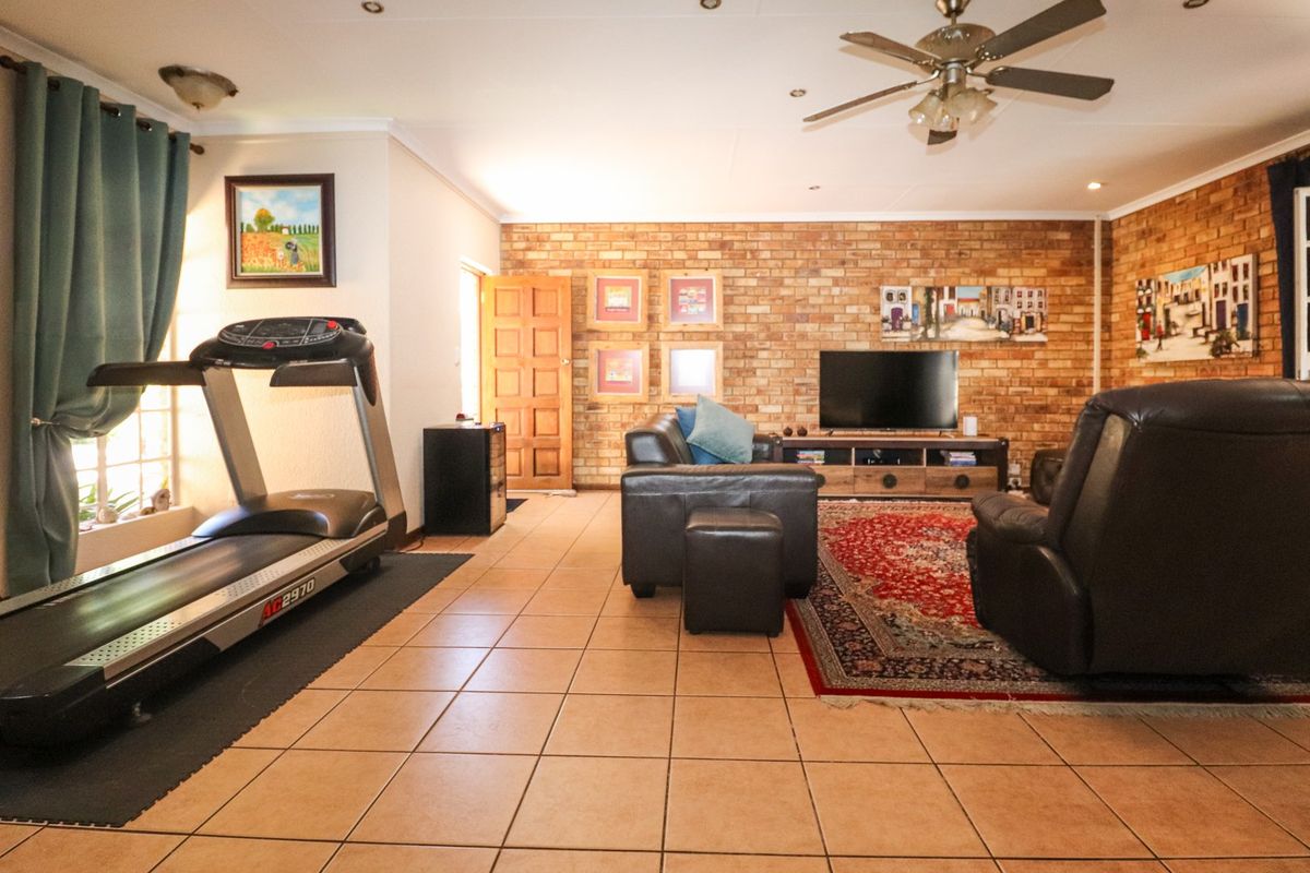 Spacious living area featuring an exposed brick feature wall, tiled flooring, and a ceiling fan, offering a warm and functional layout.
