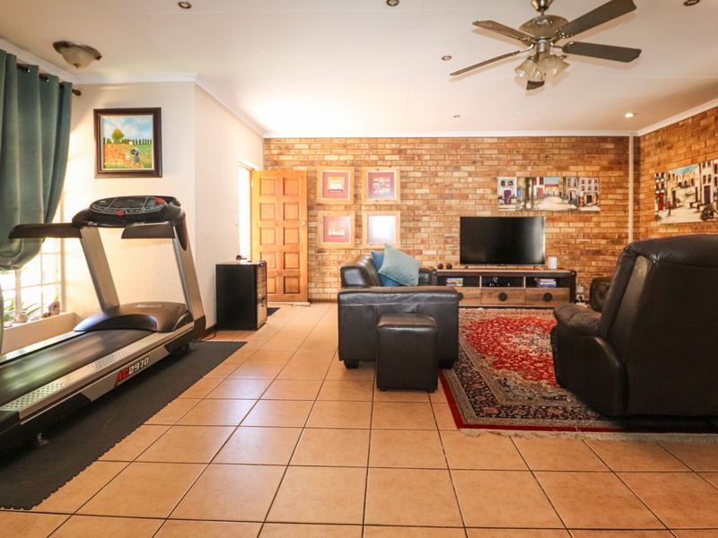 Spacious living area featuring an exposed brick feature wall, tiled flooring, and a ceiling fan, offering a warm and functional layout.
