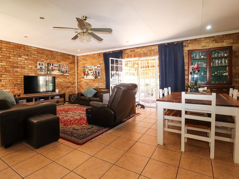 Spacious open-plan living and dining area featuring exposed brick walls, tiled flooring, and direct access to the outdoor patio through security-fitted french doors.