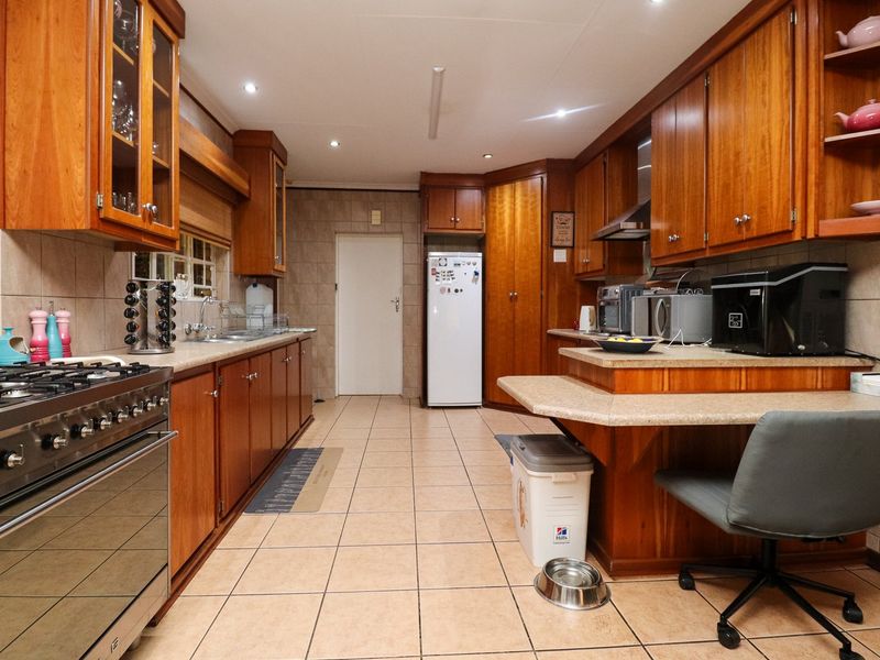 Spacious kitchen featuring extensive wooden cabinetry, a gas stove with extractor fan, tiled flooring, and a convenient breakfast bar area.