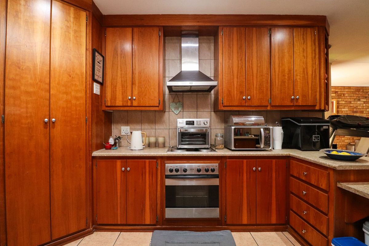 A functional kitchen featuring warm-toned wooden cabinetry, a stainless steel oven and extractor fan, stone countertops, and a tiled backsplash.