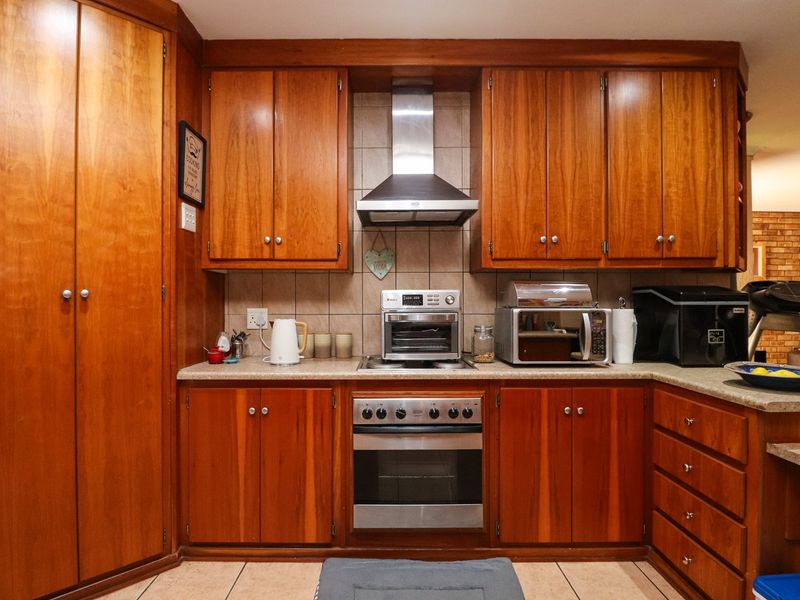 A functional kitchen featuring warm-toned wooden cabinetry, a stainless steel oven and extractor fan, stone countertops, and a tiled backsplash.