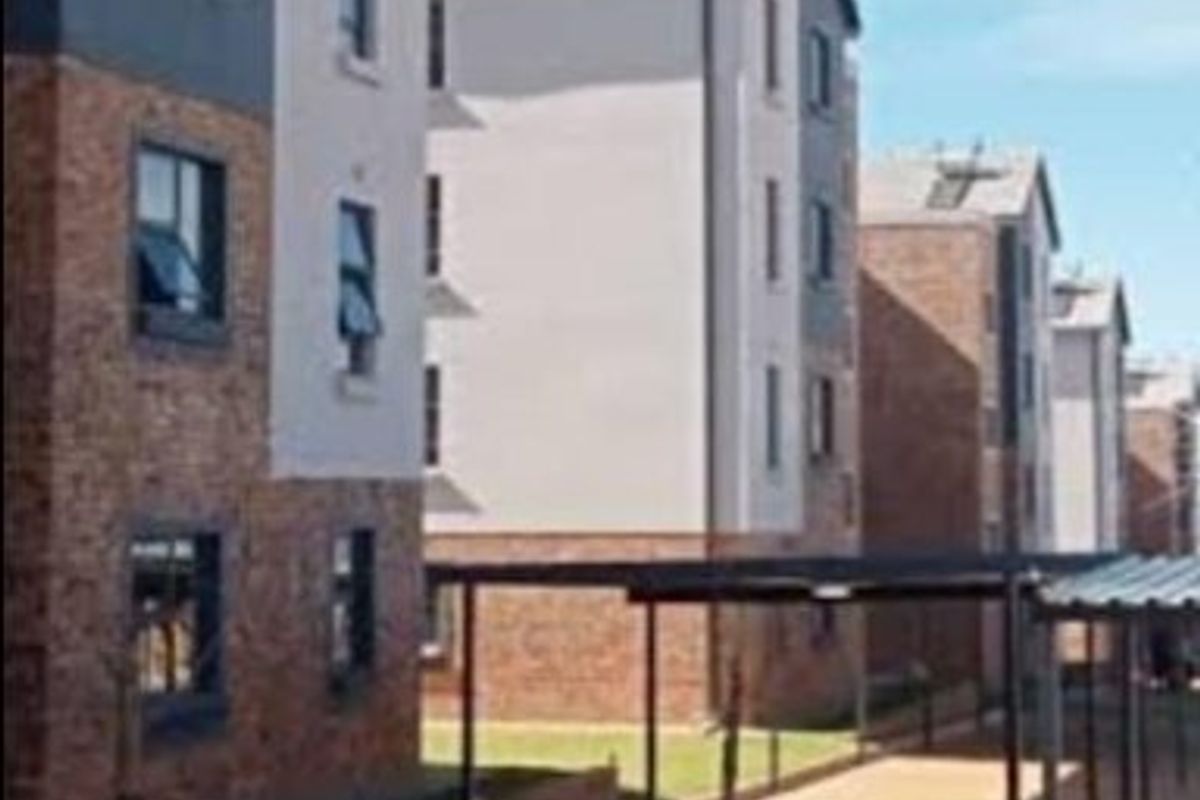 Exterior view of multi-story apartment blocks featuring brick and plaster facades, solar water heating systems, and covered parking bays.