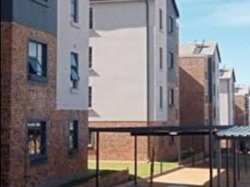 Exterior view of multi-story apartment blocks featuring brick and plaster facades, solar water heating systems, and covered parking bays.