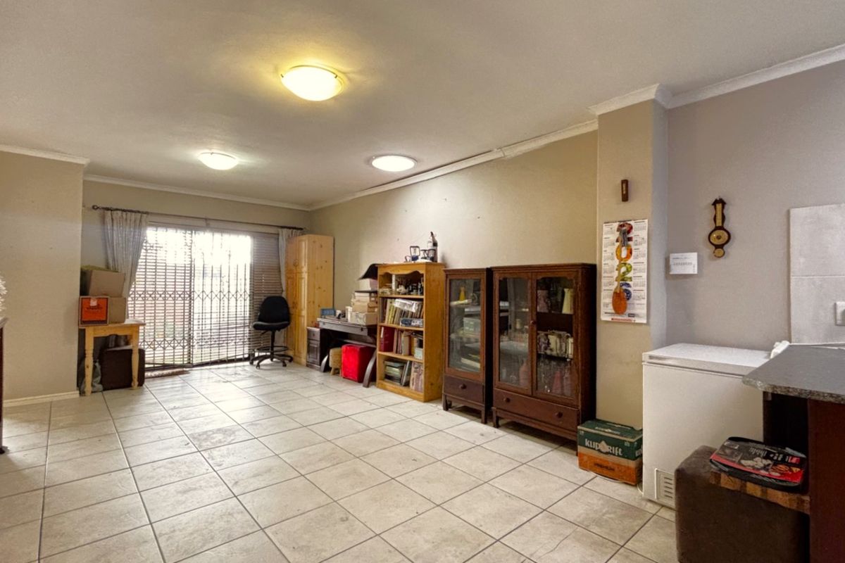 Spacious living area featuring neutral tiled flooring, ceiling lighting, and a sliding glass door with security gate providing access to the exterior.