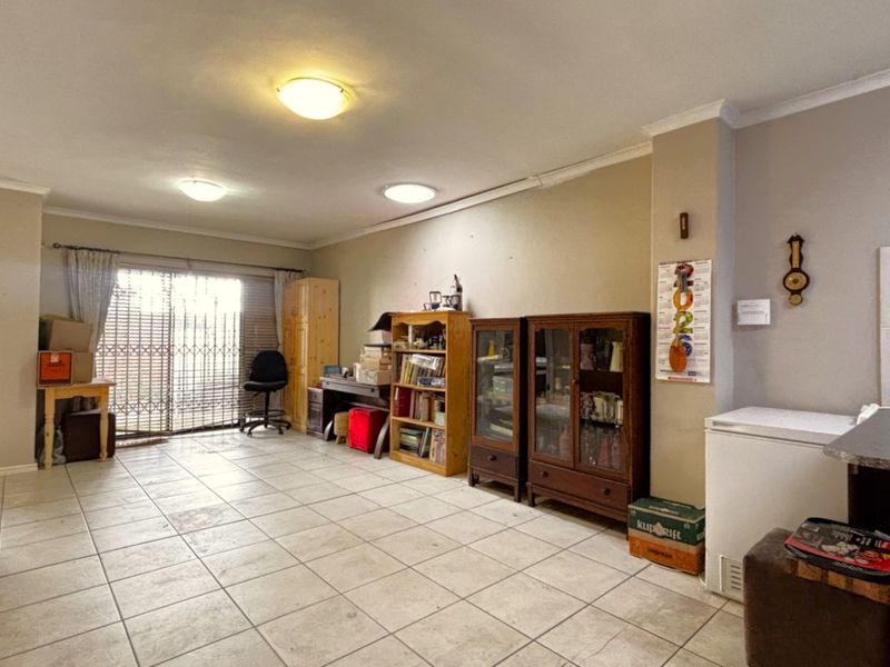 Spacious living area featuring neutral tiled flooring, ceiling lighting, and a sliding glass door with security gate providing access to the exterior.
