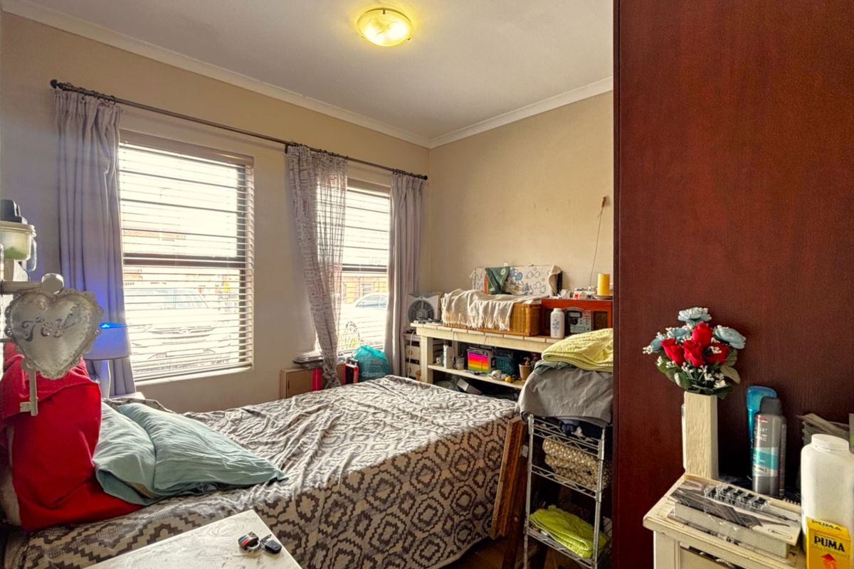 A functional bedroom featuring a built-in wardrobe, dual windows with blinds, and a central ceiling light fixture.