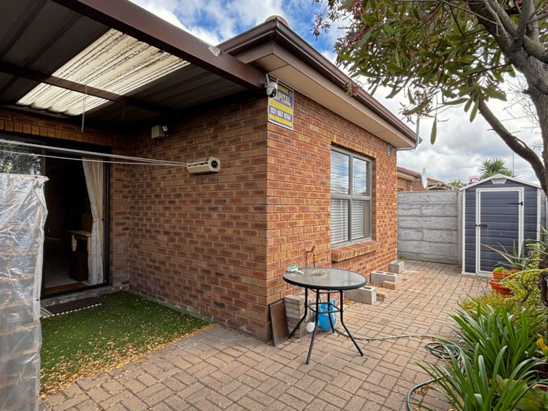Rear exterior view featuring a brick facade, covered patio area, paved courtyard, and a storage shed within a fenced garden space.
