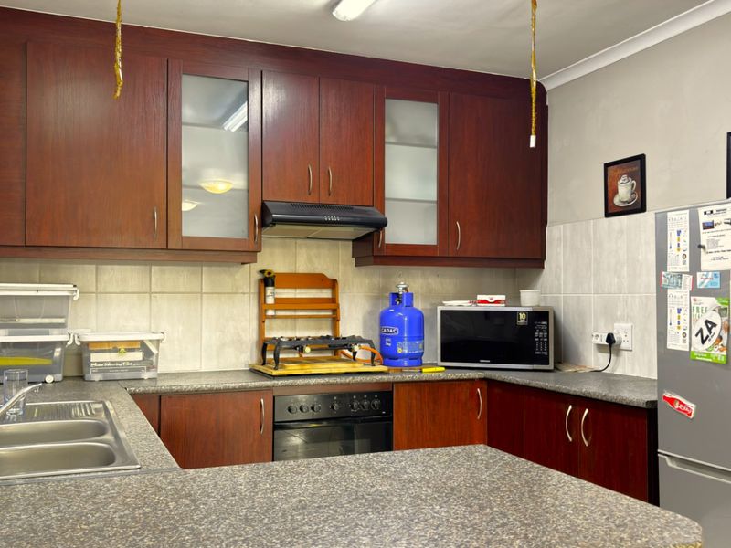 A functional kitchen featuring dark wood cabinetry, laminate countertops, a double stainless steel sink, and a built-in oven with an extractor fan.